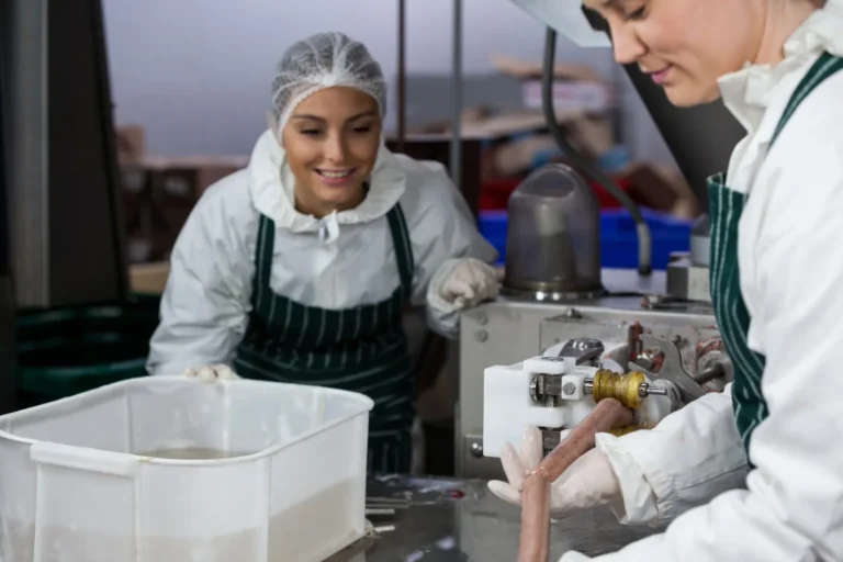 Pekerja memproses sosis di fasilitas produksi makanan dengan peralatan stainless steel yang higienis.