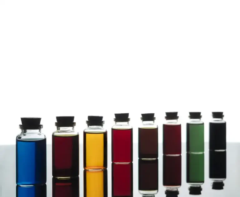 Deretan botol kecil berisi cairan warna-warni di permukaan reflektif, menyerupai pewarna makanan sintetis.
