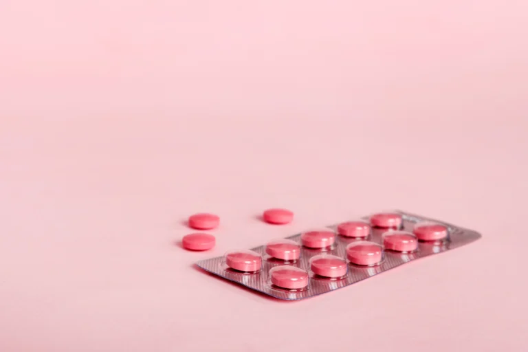 Kemasan blister berisi kapsul dan tablet vitamin berwarna-warni di atas latar belakang polos.