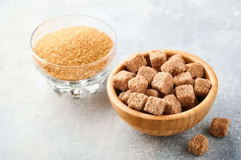 Mangkuk bambu berisi kubus gula di atas meja abu-abu, menampilkan pemanis alami sebagai bahan makanan.