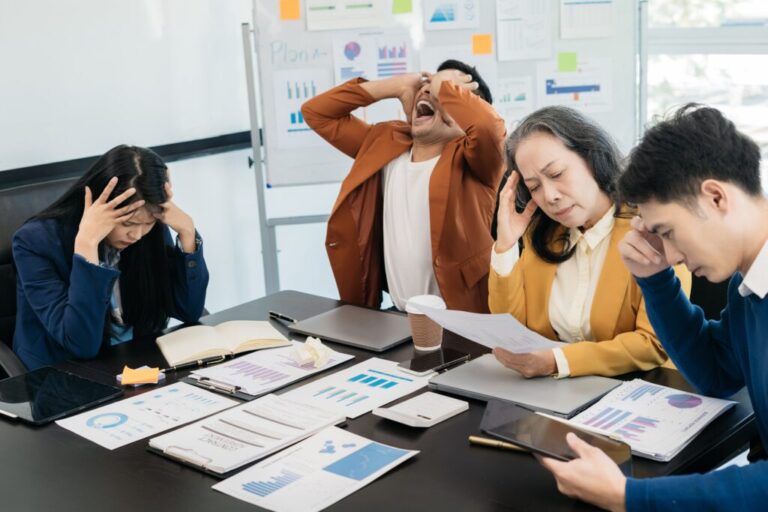 Tim bisnis duduk lesu di meja rapat sambil menatap dokumen dan berdiskusi mencari solusi masalah.