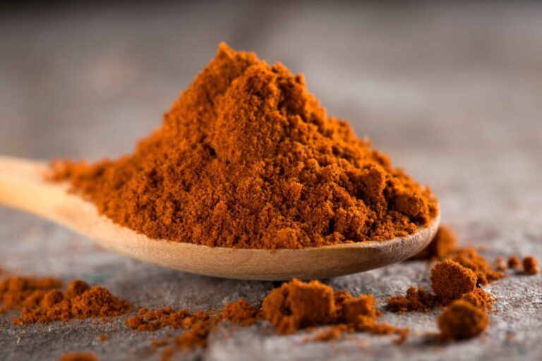 Bubuk paprika merah menyala dalam mangkuk kayu dengan cabai kering, menonjolkan warna dan tekstur bumbu.