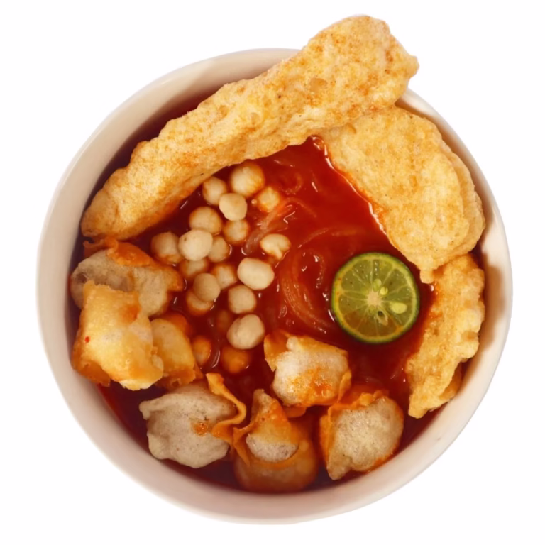 Semangkuk cuanki instan dengan kuah berbumbu, bakso kecil, tahu, dan taburan daun bawang di atas meja.